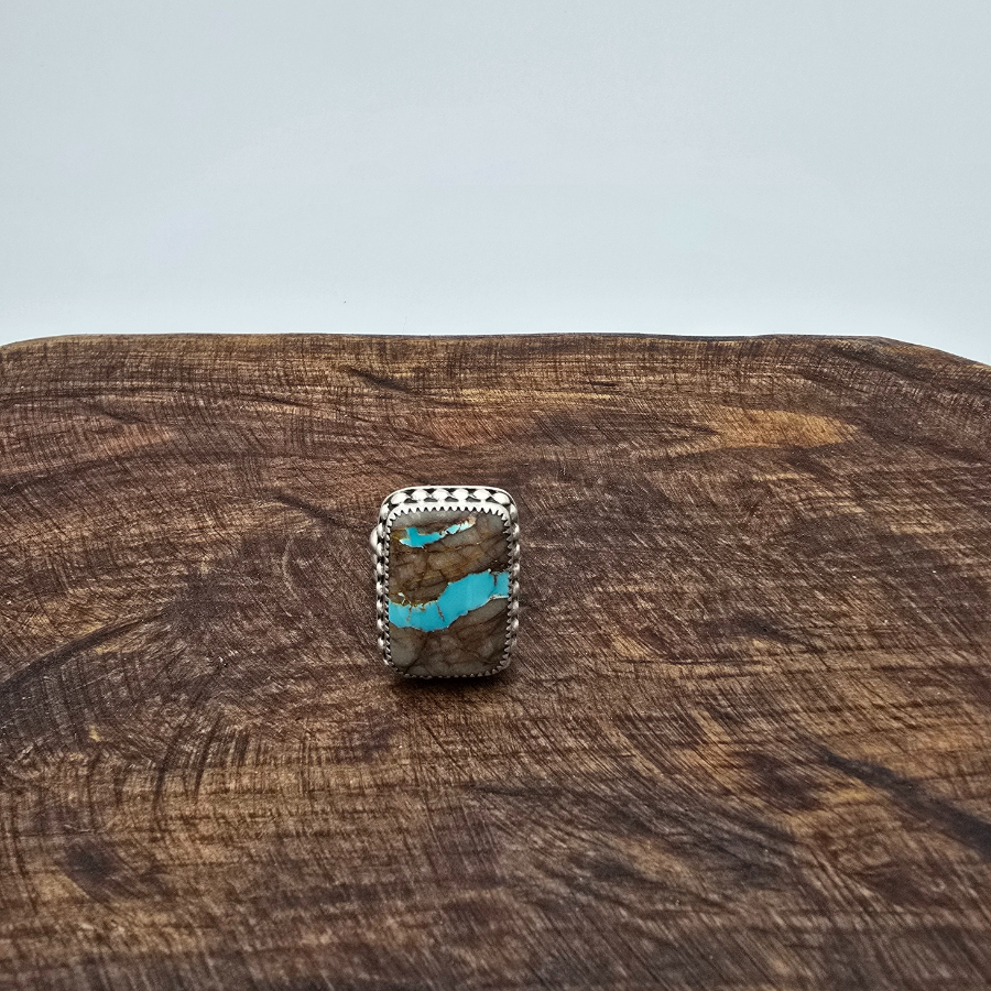 A sterling silver and turquoise ring on a wooden surface.