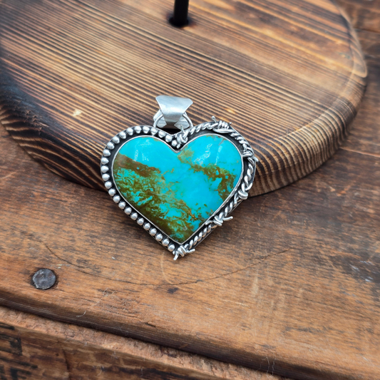 Heart-shaped turquoise pendant with silver frame on a wooden surface