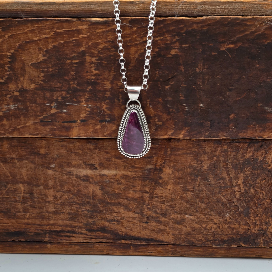 Necklace with a purple teardrop pendant on a wooden surface